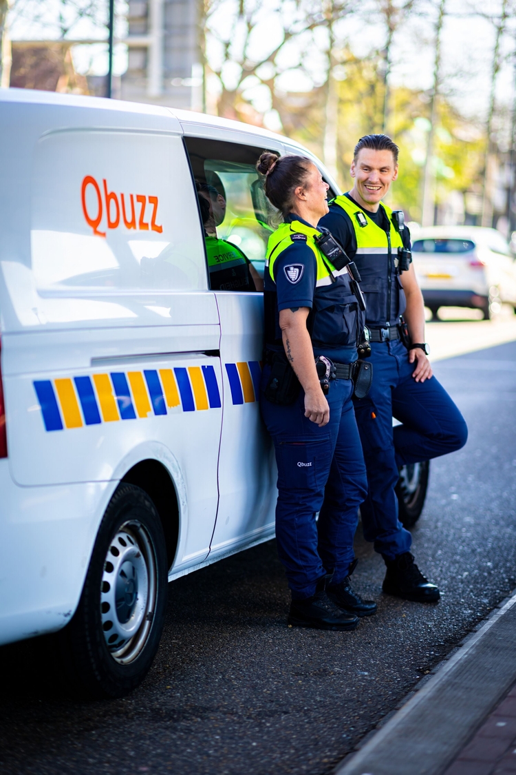 Twee Service en Veiligheid collega's leunen tegen een QBuzz werkbusje aan