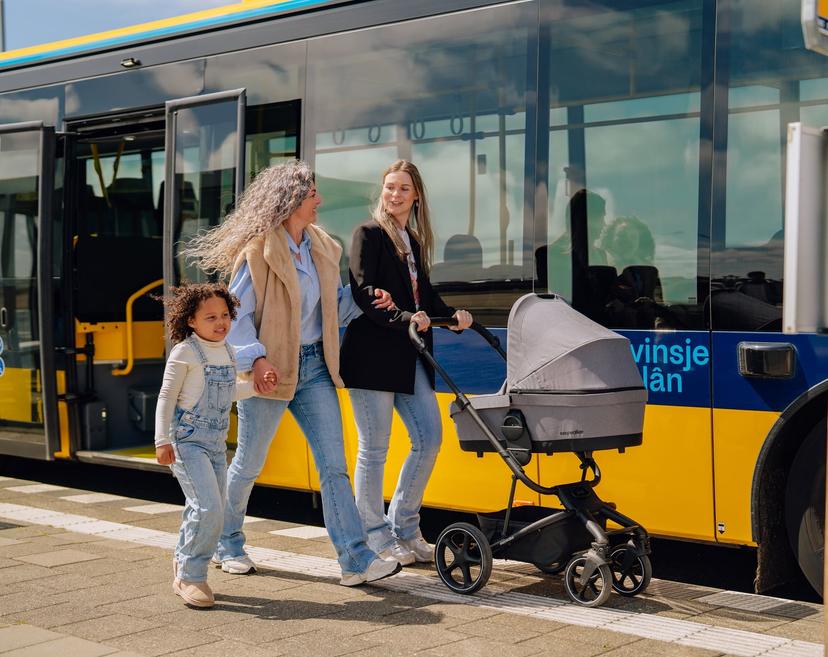 Vriendinnen bij Bushalte met kind en kinderwagen, lachend, wandelend.