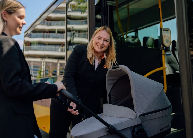 Chauffeuse helpt vrouw met kinderwagen de bus in